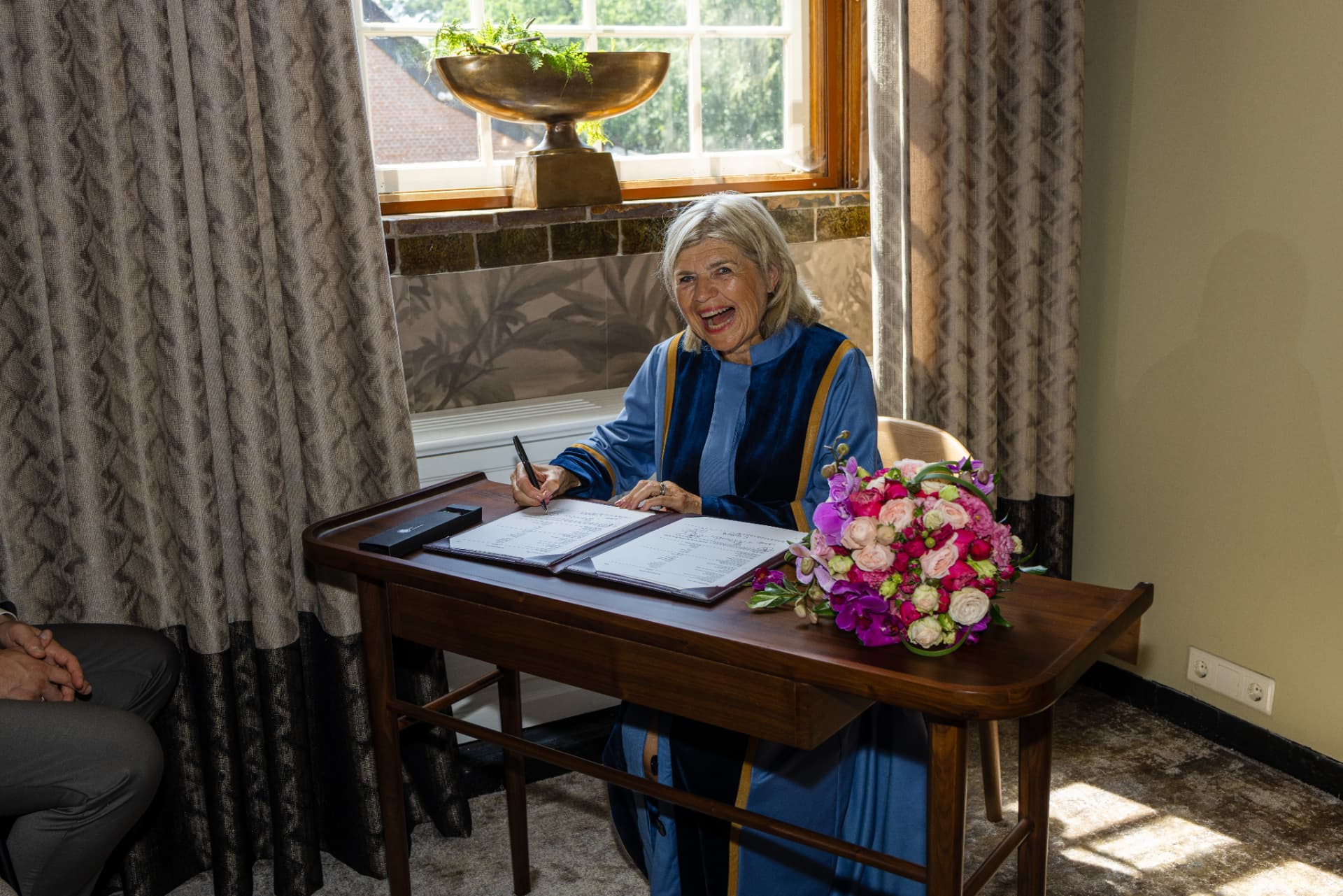 Esther tekent lachend de trouwakte aan tafel met een boeket